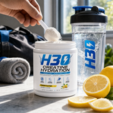 Scooping H3O creatine hydration powder into a shaker with lemon slices