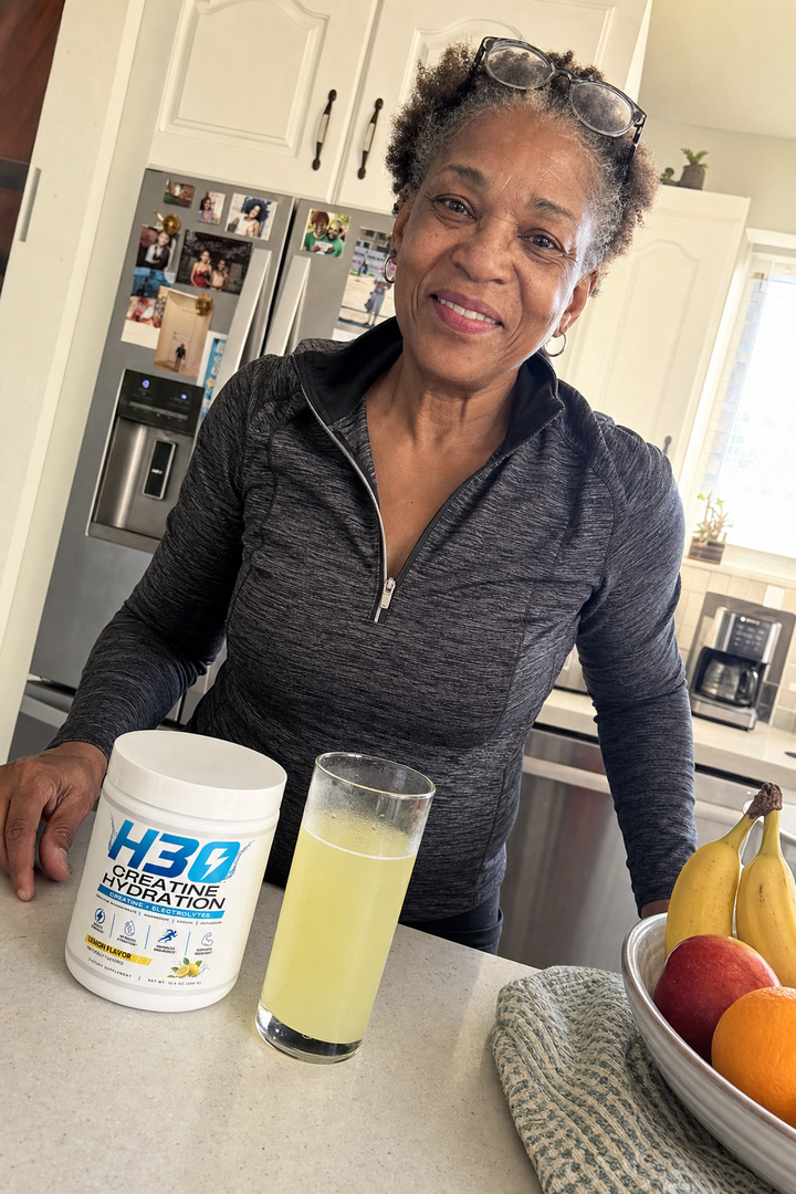 Active woman in her sixties with a glass of lemon H3O creatine drink in her kitchen